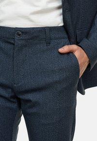 Navyblauwe broekpak met visgraatpatroon, met een vlakke voorkant, zijzakken en een knoopsluiting, gemaakt van een gebreid wol-mengsel.