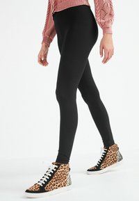 Zwarte leggings in combinatie met hoge sneakers met een luipaardprint. De leggings zijn aansluitend en gemaakt van rekbaar materiaal.