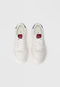 Hvide sneakers med en glat læderoverdel, ruskindsdetaljer og en gummisål. Har hvide snørebånd og et rødt og hvidt logo på tungen.