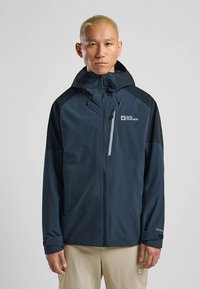 Tamsiai mėlyna nepralaidi vandeniui striukė su užtrauktuku priekyje, reguliuojama kapišonu ir kontrastingomis juodomis rankovėmis. Ypatingos savybės: logotipas ir lengvas dizainas.