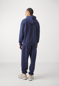 Marineblå hettegenser og tilhørende joggebukser laget av mykt stoff, med kengurulomme og en fronthette-design.