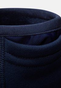 Polsino in tessuto blu navy con una superficie liscia, caratterizzato da una cucitura e un bordo ripiegato, che garantiscono una vestibilità flessibile e comfort.
