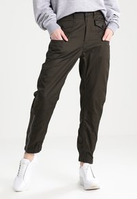 Oliwkowe spodnie cargo z tapered ankles, wieloma kieszeniami i gładką teksturą, z dodatkowymi zamkami na dolnych bokach.