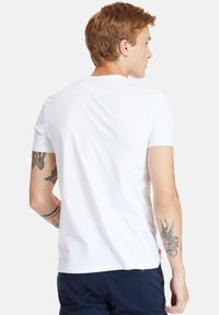 Weißes Baumwoll-T-Shirt mit kurzen Ärmeln und Rundhalsausschnitt, das über eine glatte Textur und ein kleines Etikett am Saum verfügt.