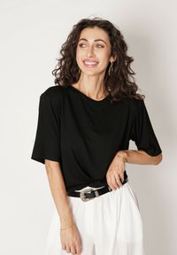 Czarny, krótki top z lekkiego materiału, o luźnym kroju i okrągłym dekolcie, zestawiony z białymi spodniami z wysokim stanem oraz czarnym paskiem.