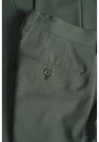 Pantalons ajustés vert foncé avec une poche arrière à bouton et des coutures soignées. Le matériau a une finition lisse et texturée.