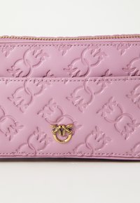 Roze neplederen portemonnee met een gegraveerd bloemenpatroon, gouden hardware logo-accent en ritsluiting. Bevat een gladde textuur en gedetailleerde stiksels.