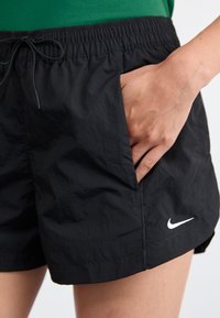 Juodi šortai pagaminti iš lengvos, tekstūruotos medžiagos. Yra elastinė juosmens juosta, reguliuojama raišteliu ir šoninės kišenės. Rodyklė Nike.