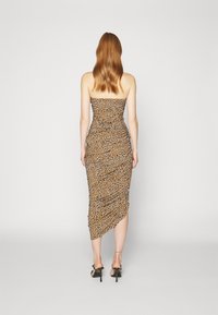 Robe sans manches en imprimé léopard avec une silhouette ajustée, taille cintrée et ourlet asymétrique. Tissu lisse avec un léger brillant. Talons noirs.