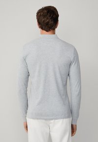 Vaaleanharmaa pitkähihainen poolopaita, jossa on kaulus, valmistettu pehmeästä kankaasta; suorareunainen helma ja istuvat hihansuut. Minimalistinen muotoilu.