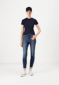 Marineblå tettsittende t-skjorte kombinert med høyt liv blå stramme jeans og hvite høyhælte sneakers. Svart caps fullfører antrekket.