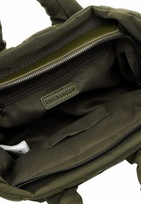 Olive green canvas tote bag interior with a zippered pocket, fabric lining, and a leather label. Features a soft texture and structured shape.