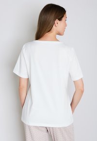 Hvid, kortærmet t-shirt med rund halsudskæring, glat tekstur og en afslappet pasform, båret med mønstrede lysegrå pyjamasbukser.