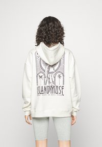 Sudadera con capucha blanca con un gran estampado gráfico negro en la espalda que presenta una sirena y palmeras. Complementada con mangas holgadas y una capucha.