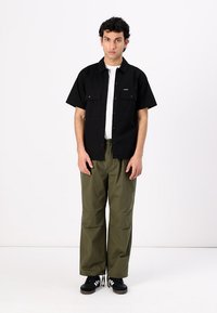 Čierne tričko s krátkym rukávom a dvoma prednými vreckami, v kombinácii s voľnými olivovými nákladnými nohavicami s vreckami a šnúrkami na leme. Čierne tenisky.