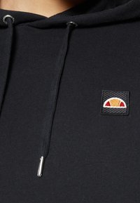 Sweat à capuche noir avec cordons et un petit logo brodé représentant un demi-cercle en jaune, rouge et blanc sur la poitrine.