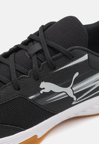 Baskets de sport noires avec une tige en maille texturée, présentant un logo et des rayures argentés, et une semelle intermédiaire blanche avec une semelle extérieure en caoutchouc couleur gomme.