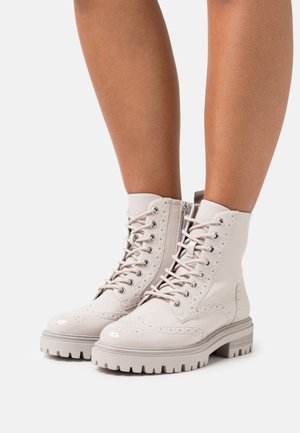 Schnürstiefeletten aus leicht cremfarbenem Leder mit Broguedekor und einer dicken, strukturierten Sohle. Verfügt über Metallösen und eine glatte Oberfläche.