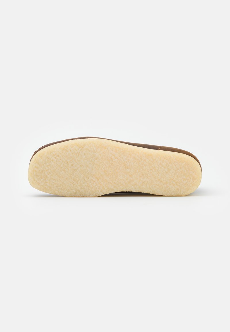 Sole of a shoe, featuring a textured cream rubber base with a brown edge. The surface is smooth with a slight sheen.
