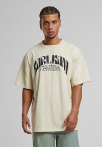 Beige, oversized póló környakú, rövid ujjú, elöl nagy, fekete felirattal: "KARL LAGERFELD INTERNATIONAL".