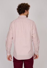 Chemise à rayures rouges et blanches à manches longues avec col boutonné, fabriquée dans un tissu à texture lisse, présentant un ourlet arrondi et des poignets boutonnés.