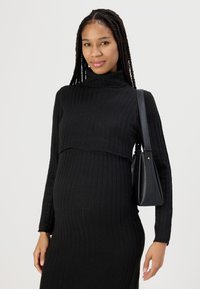 Abito nero a coste con collo alto, caratterizzato da un top corto sopra. Indossato con una borsa nera, che mette in risalto una silhouette aderente.