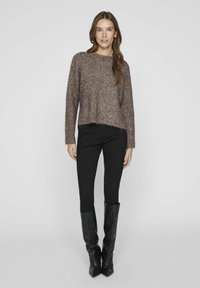 Brūns pūkains adīts džemperis ar īsu dizainu, laivu formu kakla izgriezumu un saplēstu malu, apvienots ar pieguļošiem melniem biksēm un melnām zābakiem līdz ceļiem.