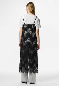 Melns mežģīņu kamzolis pār baltu T-kreklu, komplektā ar gaiši pelēkām plata COVID biksēm. Mežģīnes ir ar ziedu rakstu un vilnainu apdari.