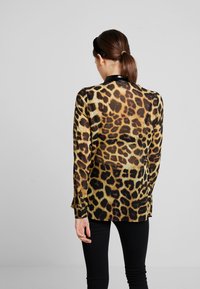 Sheer leopard-print shirt in shades of gold and black, featuring a collar and long sleeves, paired with black fitted pants.