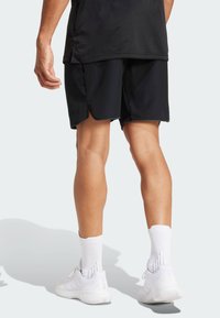 Black athletic shorts with a split hem, paired with white socks and white sneakers. Background is light gray, focusing on apparel details.