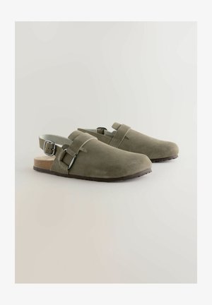 Olive green suede clogs with an open back, adjustable silver buckle strap, and brown textured sole. Minimalist design with smooth finish.