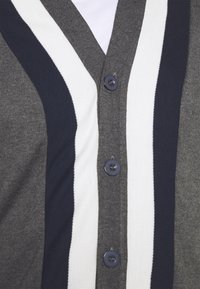 Kofta med V-ringning i grått, marinblått och vita ränder. Har fem knappar i mörkblått och en mjuk stickad textur.