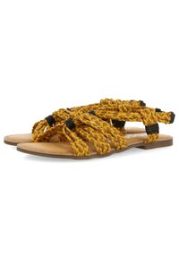 Sandalias amarillas trenzadas con suela plana, que presentan detalles en negro. El material parece tejido, con un acabado texturizado y un diseño abierto.