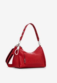 Borsa a mano in pelle rossa con forma curvata. Presenta una tasca con zip sul fronte, logo impresso e una tracolla removibile con borchie decorative.