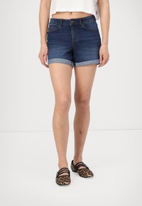 Denimshorts i mörkblått med upprullade muddar, med en framknäppning och sidofickor. Bärs med leopardmönstrade flats.