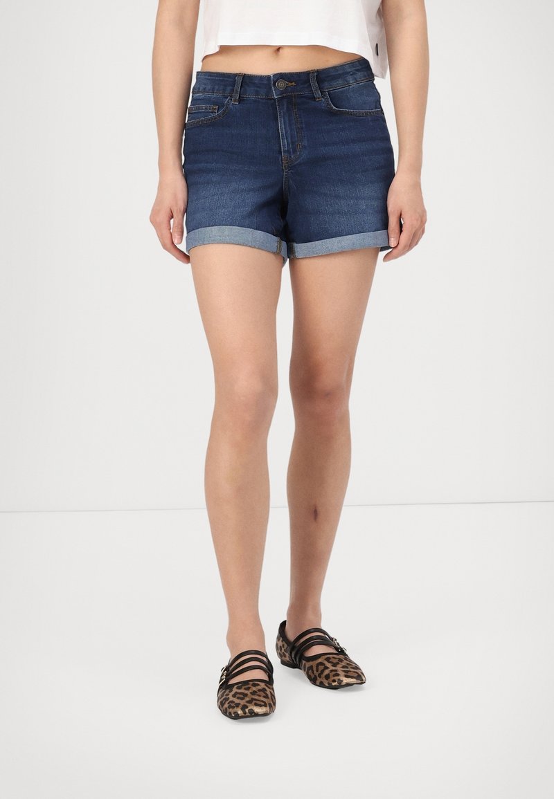 Denimshorts i mörkblått med upprullade muddar, med en framknäppning och sidofickor. Bärs med leopardmönstrade flats.