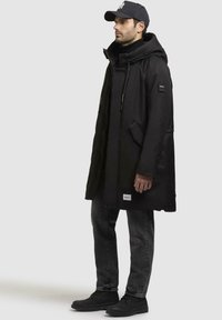 Sort, isoleret parka med høj krave, lynlåslukning og justerbare snore. Har sidelommer og et logo-patch på ærmet.