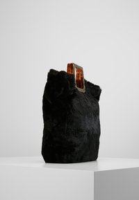 Svart väska i konstpäls med strukturerad yta, försedd med ett handtag i bärnstenfärgad akryl för en modern touch.