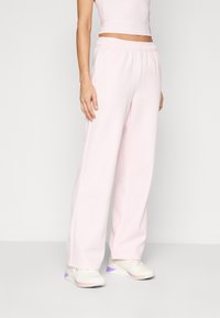 Light pink sweatpants with an elastic waistband, wide-leg fit, and soft texture. Paired with white sneakers featuring purple accents.