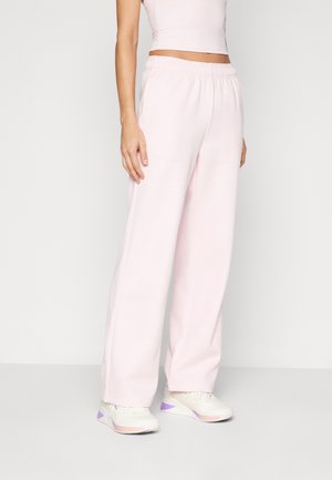 Pantalons de survêtement rose clair avec une taille élastique, coupe large et texture douce. Associés à des baskets blanches avec des accents violets.