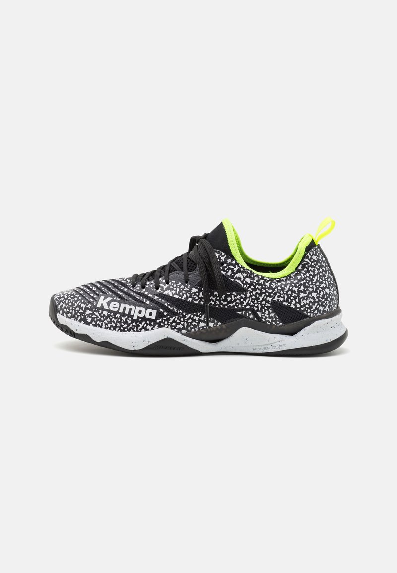 Zwart-witte atletische schoen met groene accenten, bovenkant van mesh, zwarte veters en een gestructureerde zool voor grip. Bevat merklabel aan de zijkant.