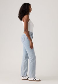 Jeans in denim azzurro chiaro con un taglio dritto, vita alta e cuciture classiche. Abbinati a una canotta bianca aderente e sneakers bianche.