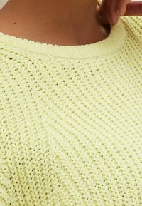 Hellgelber Strickpullover mit Rundhalsausschnitt, ausgestattet mit einem strukturierten Muster und gerippten Bündchen. Weicher Stoff und lockere Passform.