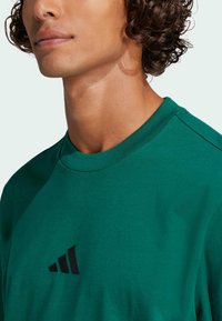 Zöld pamut póló kerek nyakkivágással és rövid ujjakkal. Elülső részén egy kis fekete Adidas logó található. Sima tapintású.