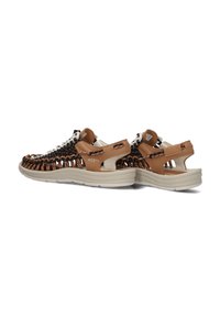 Braune und schwarze gewebte Sneakers mit einer leichten beigen Sohle, ausgestattet mit einem sicheren Rückengurt und einem minimalistischen Schnürsystem.