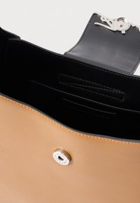 Pruun nahast käekott, millel on hõbedatooni magnetklapp, must sisemus ja korrapäraselt õmmeldud servad. Näha on mitu sisemist taskut.