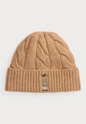 Gehaakte beanie in lichtbruin met kabeltextuur. Voorzien van een logo patch van een cartoonfiguur. Vouwrand voegt detail en warmte toe.