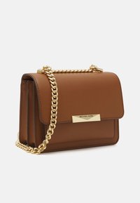 Kleine bruine leren handtas met een gouden kettingriem en een gouden sluiting met de gravure van Michael Kors, weergegeven onder een lichte hoek op een witte achtergrond.