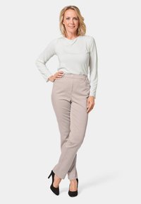 Lichtgrijze broeken met een op maat gemaakte pasvorm en knoopsluiting, gecombineerd met een langwerpig wit shirt. De schoenen zijn zwarte hakken.