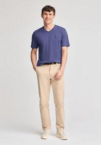 Blå kortärmad t-shirt med V-ringning, beige raka byxor och ljusfärgade sneakers. Enkelt design med en liten logotyp på tröjans bröst.